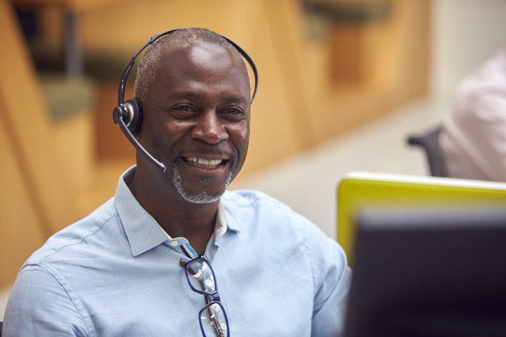 Portrait Of Mature Businessman Wearing Phone Headset Talking To Caller In Customer Services Centre Portrait Of Mature Businessman Wearing Phone Headset Talking To Caller In Customer Services Centre
